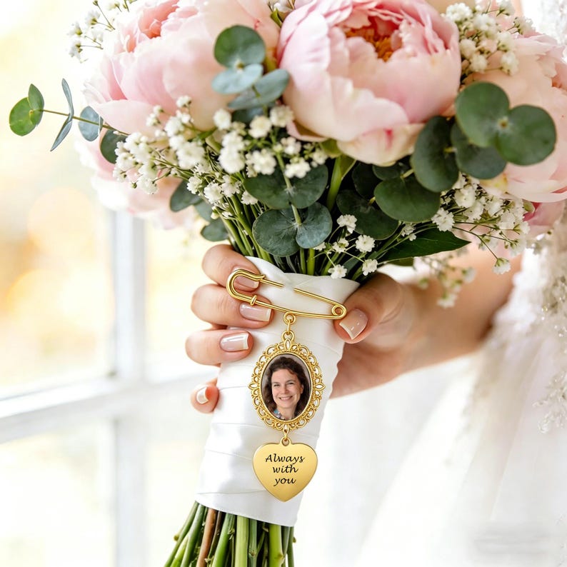 May include: A gold-toned metal brooch pin attached to a white ribbon-wrapped bouquet handle. The pin features an oval frame containing a photograph of a person and a dangling heart-shaped charm engraved with the text Always with you.