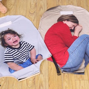 May include: Two gray, padded mats with black straps and buckles. One mat features a crying child in a black and white striped shirt and blue jeans. The other mat shows a person in a red shirt and blue jeans.
