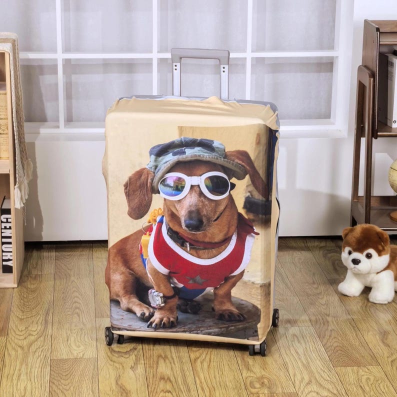 May include: A luggage cover featuring a dachshund wearing sunglasses, a camouflage hat, and a red, white, and blue vest. The dog is depicted in a photorealistic style, with a light brown background. The cover is designed to fit a standard suitcase.