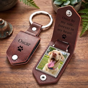 May include: A brown leather keychain with a metal ring, featuring the name Oscar and a paw print. The keychain opens to reveal a photograph of a yellow Labrador retriever and the engraved text: Once by my side, forever in my heart.