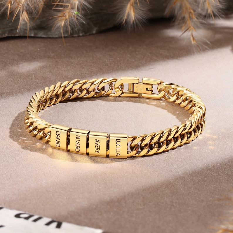 Puede incluir: Una pulsera de cadena tipo barbada en tono dorado con cuatro cuentas met&aacute;licas rectangulares, cada una grabada con un nombre: DANIEL, ALVARO, AVERY y LUCILLA. La pulsera incluye un cierre met&aacute;lico seguro y un acabado pulido en toda la pieza.