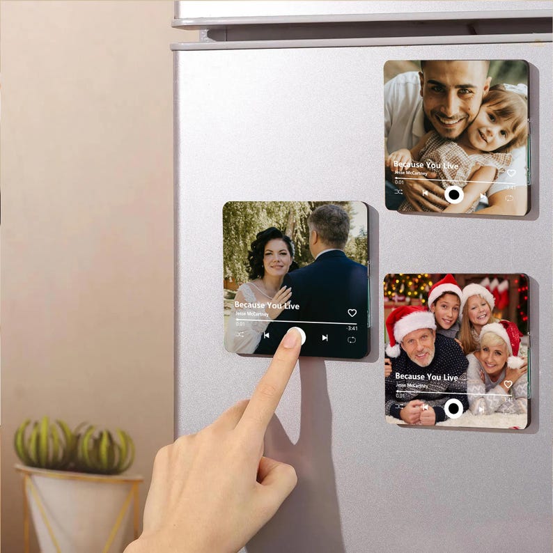 K&ouml;nnte beinhalten: Drei quadratische K&uuml;hlschrankmagnete mit individuellen Fotodrucken, die wie Musik-Player-Oberfl&auml;chen gestaltet sind. Jeder Magnet zeigt einen Songtitel, einen K&uuml;nstlernamen und Wiedergabesteuerungen sowie den Text Because You Live.