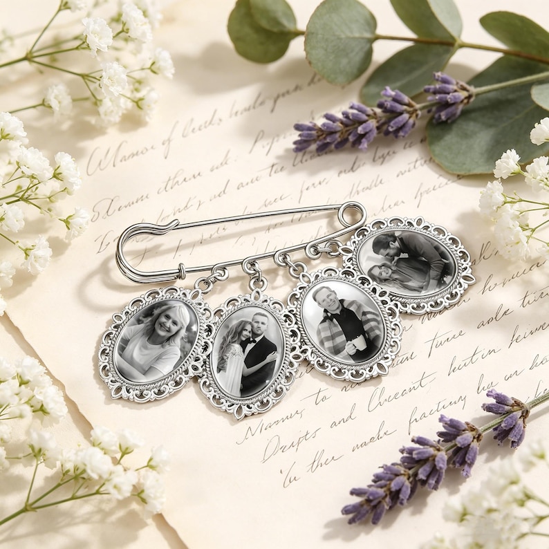 May include: A silver-toned metal safety pin brooch featuring four oval-shaped, ornate filigree frames dangling from the bottom. Each frame contains a black and white photograph of different individuals, showcasing portraits and a couple.