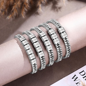 Puede incluir: Cinco pulseras de cadena tipo barbada en tono plateado con cuentas met&aacute;licas rectangulares grabadas con varios nombres, incluyendo Selena, Lucilla, Avery, Carter, Matthew, Jackson, Alvaro y Daniel. Las pulseras est&aacute;n dispuestas en fila sobre un soporte cil&iacute;ndrico.