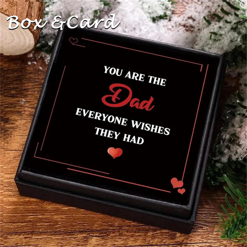 May include: A square black gift box containing a card with white and red text that reads: YOU ARE THE Dad EVERYONE WISHES THEY HAD. The card features a red heart icon below the text and a thin red border line on a black background.