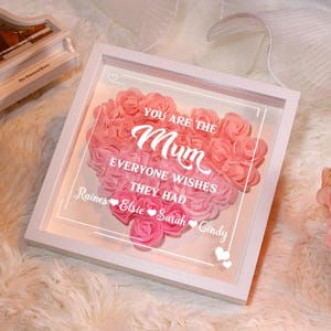 May include: White framed shadow box with a pink heart-shaped arrangement of artificial roses. The text "You are the Mum everyone wishes they had" is printed on the glass. The names "Raines, Elsie, Sarah, Cindy" are printed below the text.