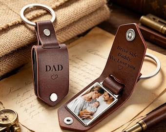 May include: Two brown leather keyrings. One keyring has the word "DAD" and a heart symbol. The other keyring has a photo and the text "Drive Safe Daddy. We Love you" with a heart symbol. Both keyrings have a silver key ring.