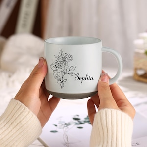 May include: White ceramic mug with a black outline of a flower bouquet and the name "Sophia" printed on the side.