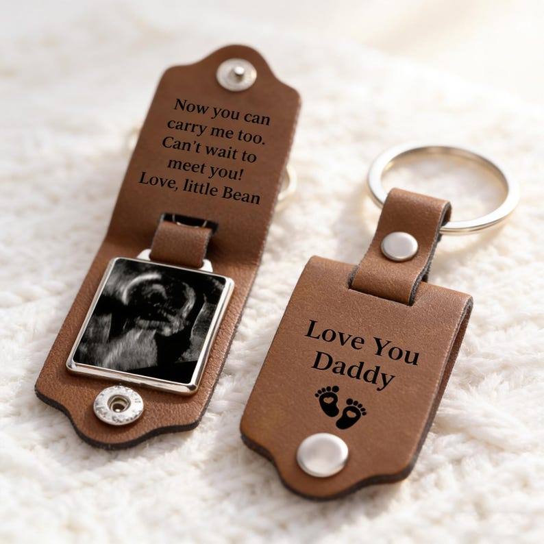 May include: Two brown leather keychains with silver metal rings. One keychain is open, revealing a black and white ultrasound image and the text: Now you can carry me too. Can't wait to meet you! Love, little Bean. The other reads: Love You Daddy.