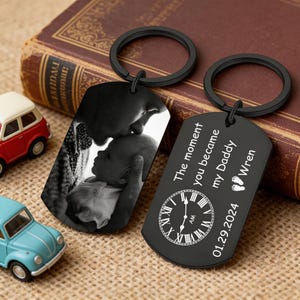 Op de afbeelding: Een witte keramische mok met een zwarte handgreep en de tekst "But First, Coffee" in een vetgedrukte, zwarte letter. De mok staat tegen een vage achtergrond, wat een gezellige setting suggereert.