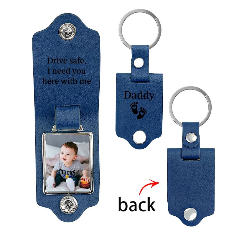 May include: A blue leather keychain with a metal ring and snap closure. The interior features a photo of a baby and the engraved text "Drive safe, I need you here with me." The exterior is engraved with "Daddy" and two small baby footprints.