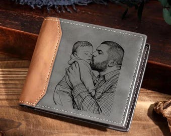 May include: A bi-fold wallet featuring a tan leather side panel and a gray panel engraved with a black line-art illustration of a person holding a baby. The wallet has visible white stitching along the edges and a rectangular, structured shape.