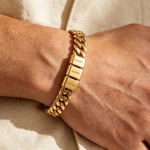 Puede incluir: Una pulsera de cadena tipo barbada en tono dorado con tres eslabones met&aacute;licos rectangulares y lisos grabados con los nombres ALVARO, AVERY y LUCILA. La pulsera consta de eslabones pulidos entrelazados alrededor de la mu&ntilde;eca.