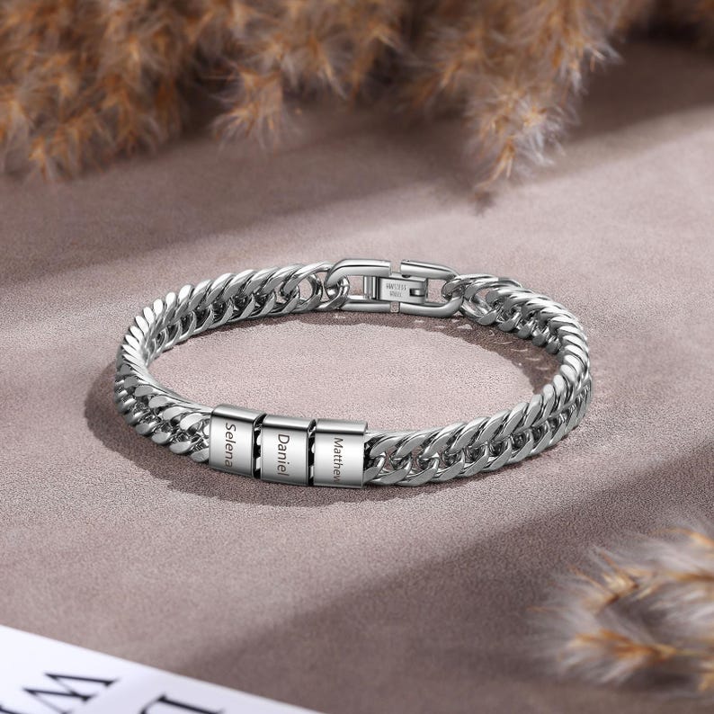 Puede incluir: Una pulsera de cadena de eslabones de metal plateado con tres cuentas rectangulares grabadas con los nombres Selena, Daniel y Matthew. La pulsera incluye un cierre de metal seguro y un acabado pulido, creando un accesorio elegante y duradero.