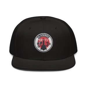 May include: A black snapback cap featuring a circular embroidered patch on the front. The patch displays a red circle background with a black SR-71 Blackbird aircraft silhouette, a small skunk graphic, and the text BLACKBIRD SR-71 3+.