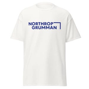 May include: A white t-shirt with the words "NORTHROP GRUMMAN" printed in blue. The text is centered on the front of the shirt, with a blue line and a right angle design element to the right of the text.