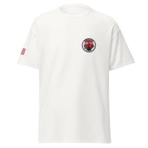 May include: A white short-sleeve t-shirt featuring a circular patch on the left chest with a black SR-71 Blackbird aircraft silhouette over a red circle, surrounded by the text BLACKBIRD SR-71 3+. A small American flag is printed on the right sleeve.