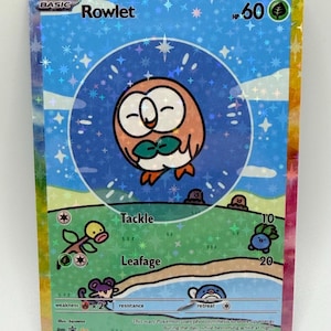 May include: A holographic Rowlet trading card featuring a round brown bird character in a blue circle. The card displays 60 HP, grass energy, and attacks Tackle and Leafage. The background shows a green landscape with small creatures and a pond.