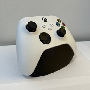 May include: A white Xbox Series X controller with black buttons and a black base. The controller is on a white surface.