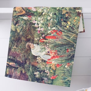 May include: A decorative kitchen towel featuring a vintage painting of a woman in a garden. The artwork showcases a woman in a white dress surrounded by vibrant red, white, and pink flowers. The towel is folded over a white shelf.