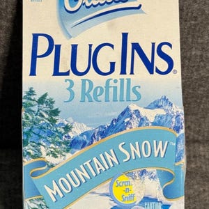 May include: A Glade PlugIns air freshener refill box with a Mountain Snow scent. The box is white and blue, featuring a mountain landscape design. It contains 3 refills and has a "NEW" sticker.