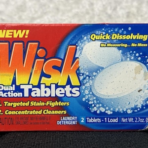 May include: A red and blue box of Wisk Dual Action Tablets laundry detergent. The box features the text "NEW!" and "Quick Dissolving." It contains two tablets and weighs 2.7 oz.