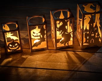 May include: Four wooden Halloween lanterns with cut-out designs of a pumpkin, bat, witch, and haunted house. The lanterns are lit from within, casting a warm glow and shadows on the wooden surface.