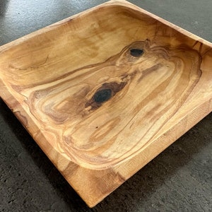 Könnte beinhalten: Eine quadratische Holzschale mit natürlicher Holzmaserung. Die Schale hat einen tiefen, abgerundeten Innenraum und einen leicht erhöhten Rand.