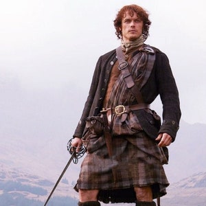 Könnte beinhalten: Ein Mann in einem traditionellen schottischen Kilt mit einem karierten Muster, einer schwarzen Jacke und einem braunen Ledergürtel. Er hält ein Schwert in seiner rechten Hand und steht auf einem felsigen Vorsprung mit einer Berglandschaft im Hintergrund.