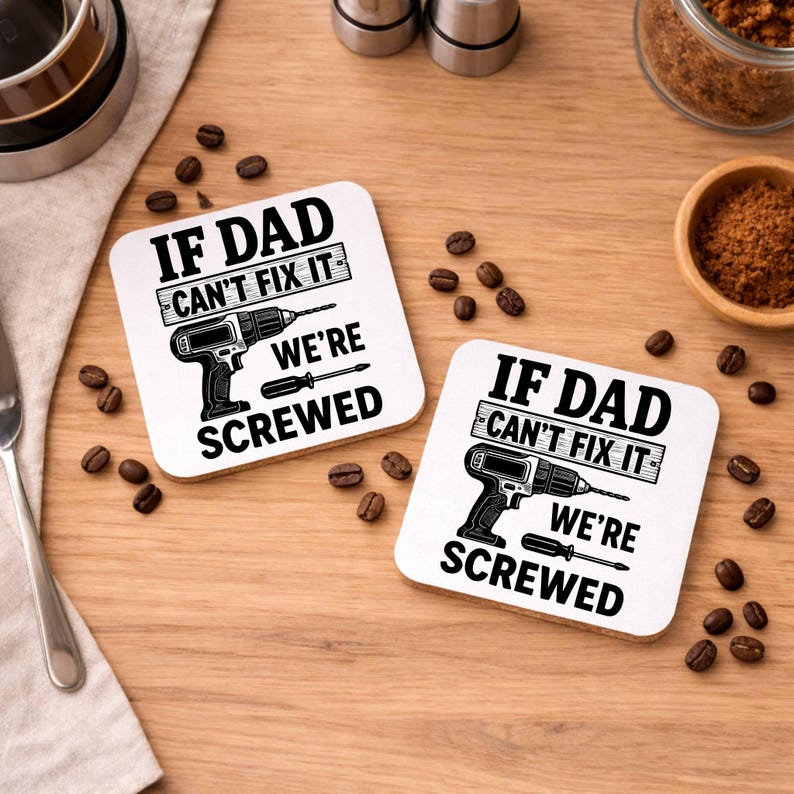 May include: Two square white coasters with the text "IF DAD CAN'T FIX IT WE'RE SCREWED" in black. Each coaster features a black illustration of a drill and a screwdriver. Coffee beans and other items are scattered around the coasters.