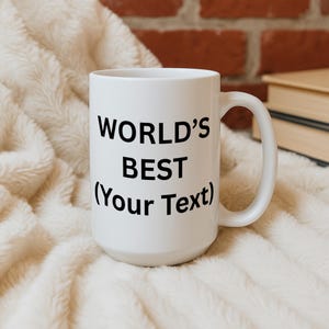 Puede incluir: Una taza de cer&aacute;mica blanca con el texto "WORLD'S BEST (Your Text)" en negro. La taza tiene un asa grande y est&aacute; sobre una superficie suave, blanca y texturizada. Una pared de ladrillos y libros est&aacute;n en el fondo.