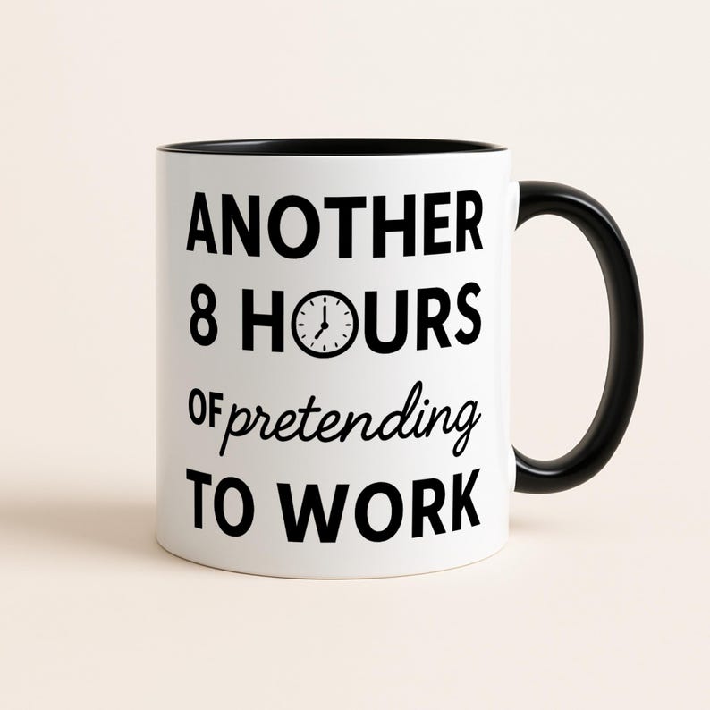 May include: White ceramic mug with a black interior and handle. The mug features the text "ANOTHER 8 HOURS of pretending TO WORK" in black, with a clock graphic. The mug is on a neutral background.