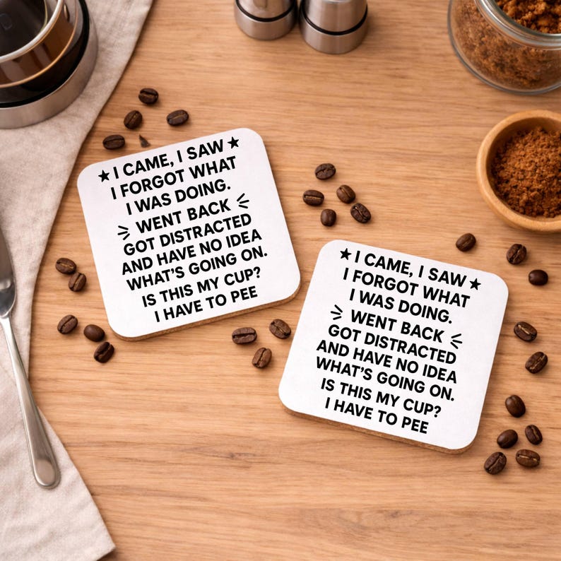 K&ouml;nnte beinhalten: Zwei quadratische wei&szlig;e Untersetzer mit humorvollem Text, darunter "I CAME, I SAW, I FORGOT WHAT I WAS DOING". Kaffeebohnen und kleine Schalen sind auf einer Holzoberfl&auml;che um die Untersetzer herum verstreut.