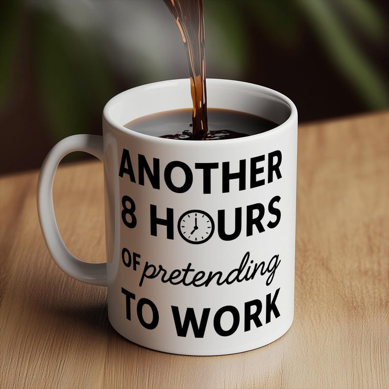 K&ouml;nnte beinhalten: Wei&szlig;e Keramik-Kaffeetasse mit dem Text "ANOTHER 8 HOURS of pretending TO WORK" in Schwarz. Dunkler Kaffee wird in die Tasse gegossen. Die Tasse hat einen Henkel und steht auf einer Holzoberfl&auml;che.