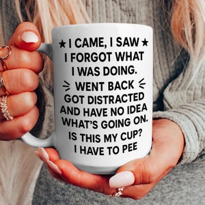K&ouml;nnte beinhalten: Wei&szlig;er Keramikbecher mit einem schwarzen humorvollen Zitat: "I CAME, I SAW, I FORGOT WHAT I WAS DOING. WENT BACK, GOT DISTRACTED AND HAVE NO IDEA WHAT'S GOING ON. IS THIS MY CUP? I HAVE TO PEE."