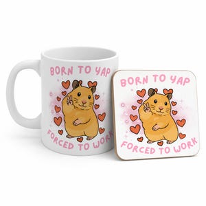 May include: White ceramic mug and square coaster set. Both feature a cartoon hamster with a peace sign, surrounded by hearts. The text reads "BORN TO YAP, FORCED TO WORK" in pink. A fun, whimsical gift set.