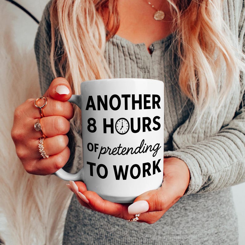 K&ouml;nnte beinhalten: Wei&szlig;e Keramik-Tasse mit dem Text "ANOTHER 8 HOURS of pretending TO WORK" in Schwarz. Die Tasse hat eine Uhr-Grafik. Die Tasse wird von einer Person mit Ringen gehalten.