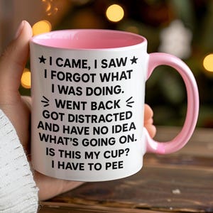 K&ouml;nnte beinhalten: Wei&szlig;er Keramikbecher mit rosa Innenraum und Henkel. Der Becher zeigt den Text "I CAME, I SAW, I FORGOT WHAT I WAS DOING. WENT BACK, GOT DISTRACTED AND HAVE NO IDEA WHAT'S GOING ON. IS THIS MY CUP? I HAVE TO PEE."