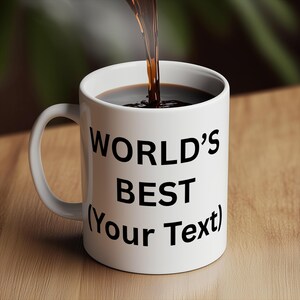 Puede incluir: Una taza de cer&aacute;mica blanca con el texto "WORLD'S BEST (Your Text)" en negro. Se vierte l&iacute;quido oscuro en la taza. La taza tiene un asa curva y est&aacute; sobre una superficie de madera.