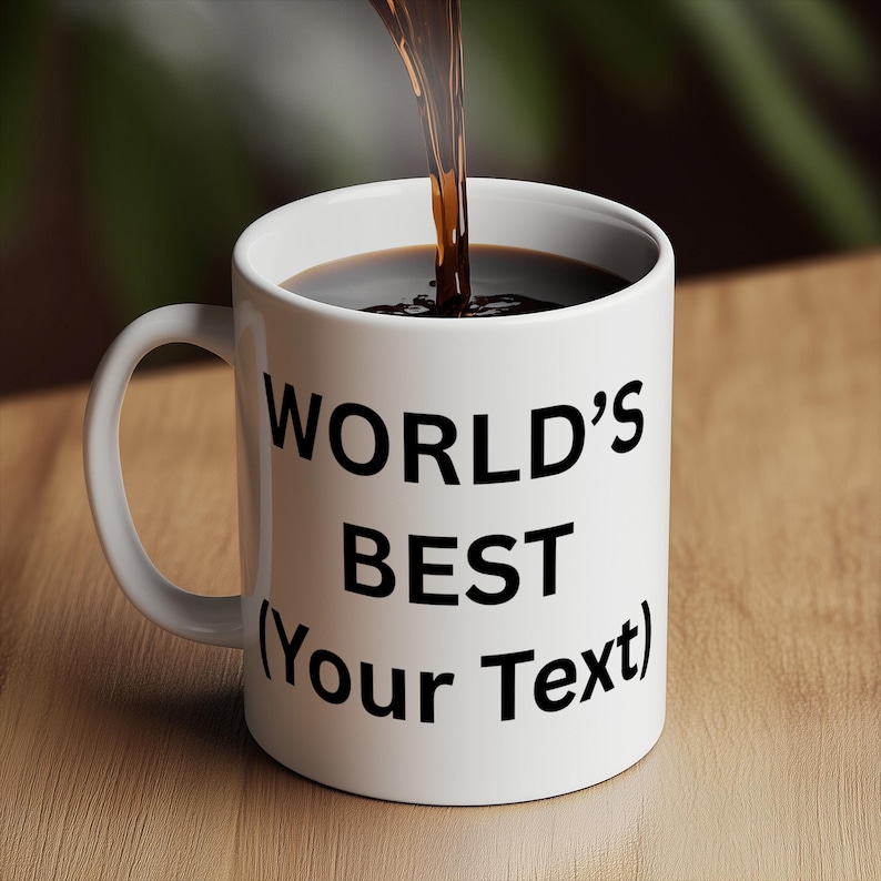 Puede incluir: Una taza de cer&aacute;mica blanca con el texto "WORLD'S BEST (Your Text)" en negro. Se vierte l&iacute;quido oscuro en la taza. La taza tiene un asa curva y est&aacute; sobre una superficie de madera.