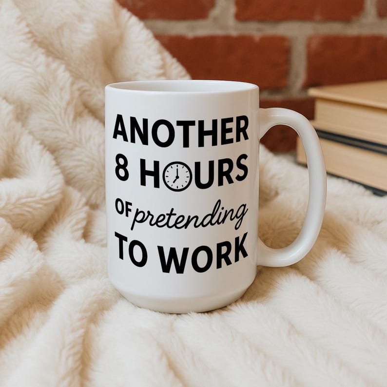 K&ouml;nnte beinhalten: Wei&szlig;e Keramik-Tasse mit dem schwarzen Text "ANOTHER 8 HOURS of pretending TO WORK". Die Tasse hat eine Uhr-Grafik und einen gebogenen Henkel. Die Tasse steht auf einer wei&szlig;en, flauschigen Oberfl&auml;che.