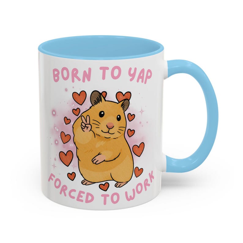 May include: White ceramic mug with a light blue interior and handle. The mug features a cartoon hamster with a peace sign, surrounded by hearts, and the text "BORN TO YAP FORCED TO WORK" in pink.
