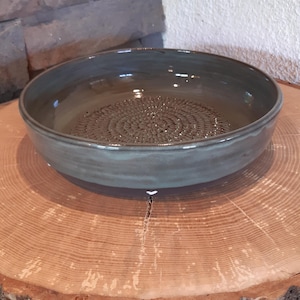 Könnte beinhalten: Eine handgefertigte, dunkelblaue Keramikschale mit einem strukturierten, kreisförmigen Muster in der Mitte. Die Schale steht auf einer natürlichen Holzscheibe und zeigt ihren rustikalen Charme. Der Rand der Schale ist glatt und leicht erhöht.