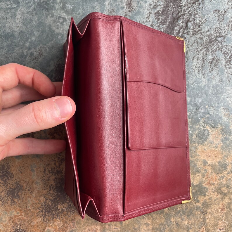 May include: A burgundy leather wallet with gold accents. The wallet is open and shows multiple card slots and a pocket for bills.