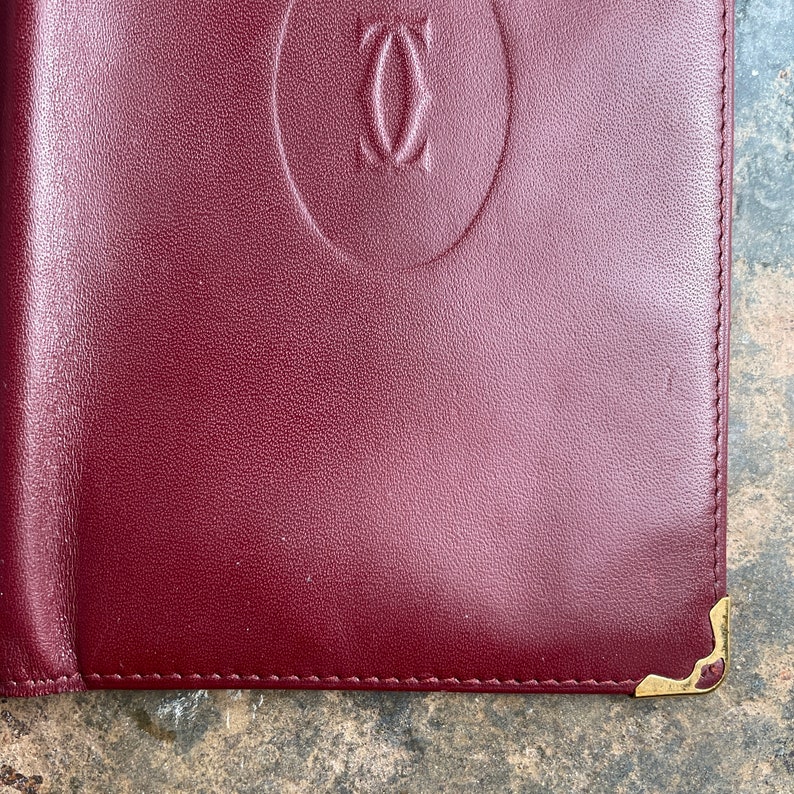 May include: A burgundy leather wallet with a gold embossed logo that reads 'Cartier'.