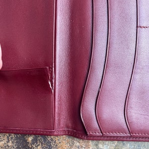May include: A burgundy leather wallet with a visible tear in the leather. The wallet has multiple card slots and a fold-over closure.