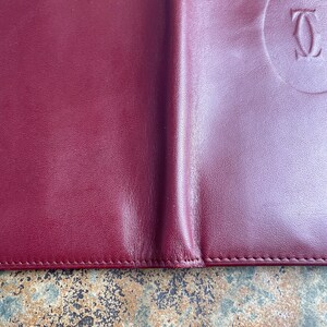 May include: A burgundy leather wallet with a stitched edge and a circular embossed logo that reads 'CARTIER'.