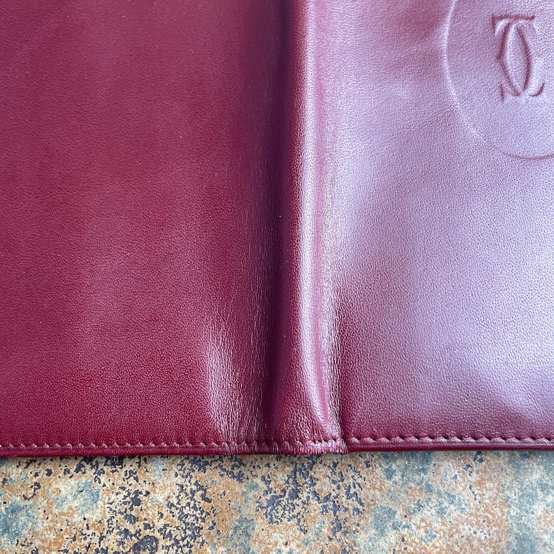 May include: A burgundy leather wallet with a stitched edge and a circular embossed logo that reads 'CARTIER'.