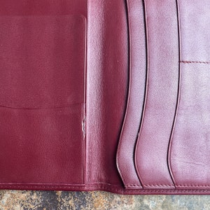 May include: A burgundy leather wallet with multiple card slots and a pocket for cash. The wallet is folded in half and the inside is visible.