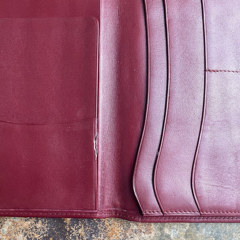 May include: A burgundy leather wallet with multiple card slots and a pocket for cash. The wallet is folded in half and the inside is visible.